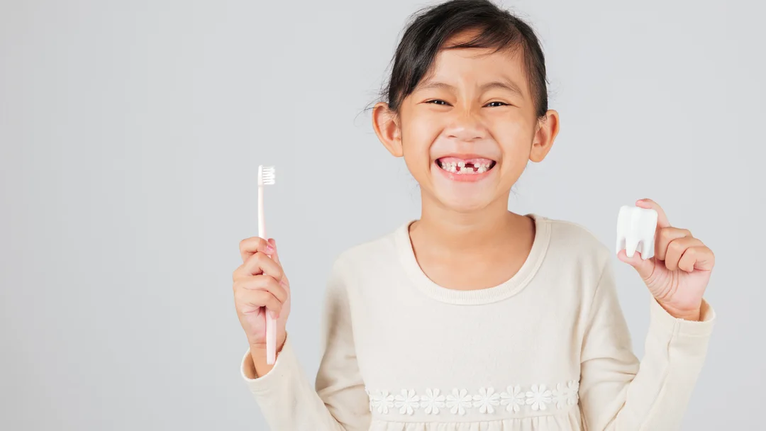 A young patient smiling at Streetsboro Dental Partners, holding a toothbrush and a model tooth